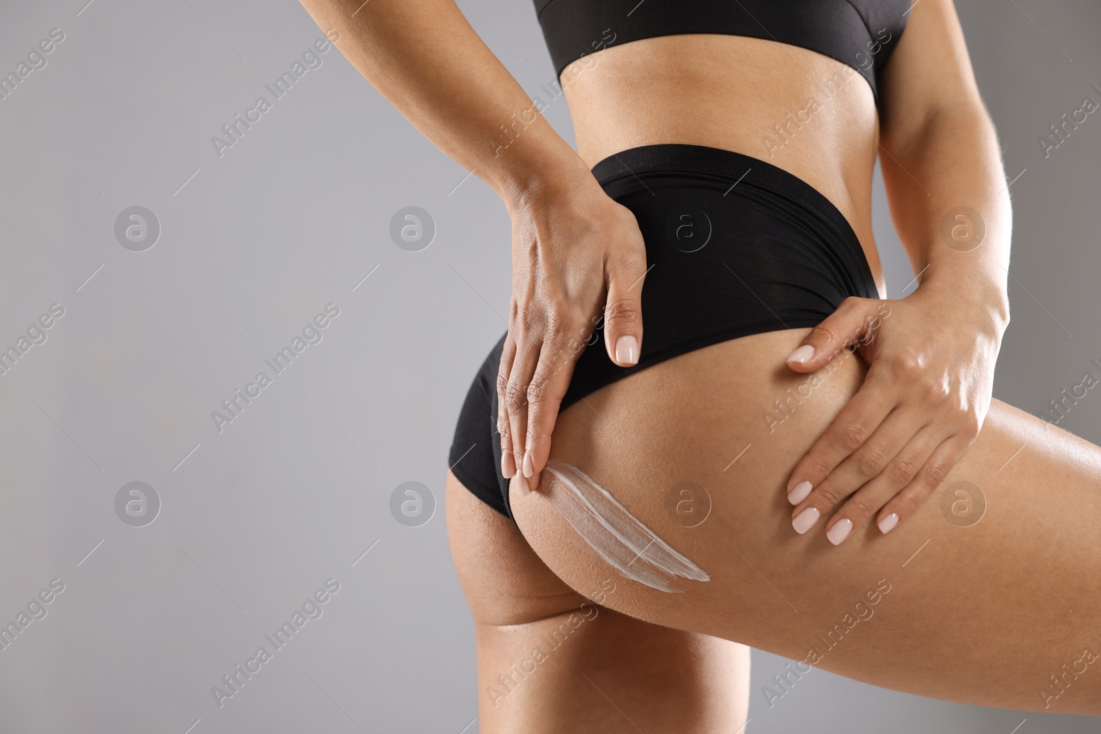 Photo of Woman applying anti cellulite cream on grey background, closeup. Space for text