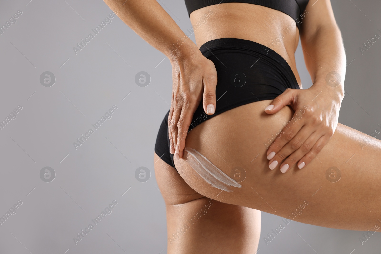 Photo of Woman applying anti cellulite cream on grey background, closeup. Space for text