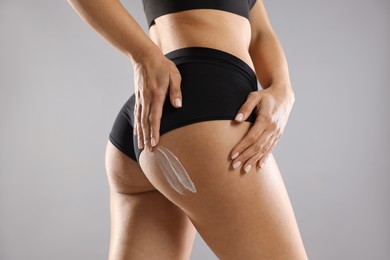 Woman applying anti cellulite cream on grey background, closeup