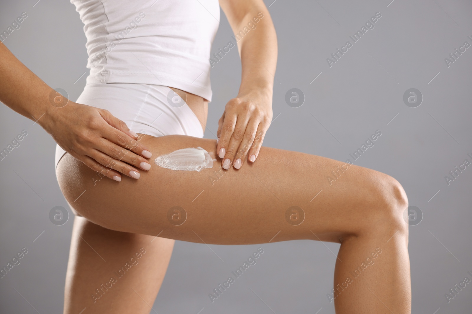 Photo of Woman applying anti cellulite cream on grey background, closeup