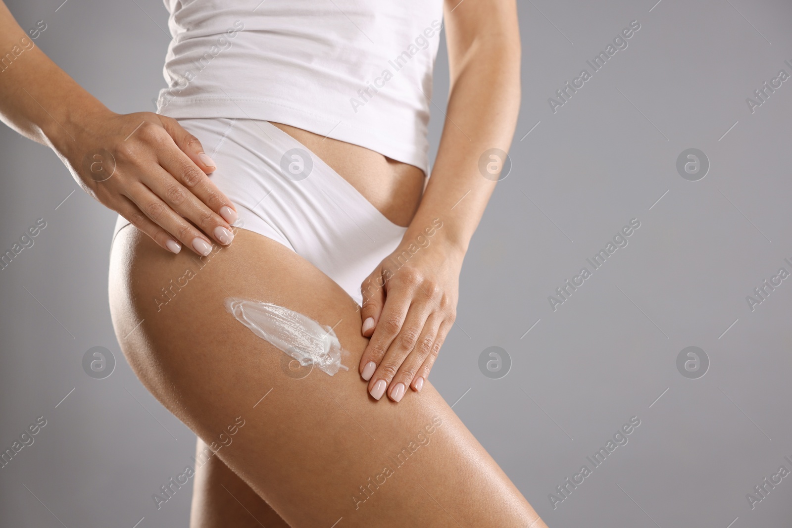 Photo of Woman applying anti cellulite cream on grey background, closeup