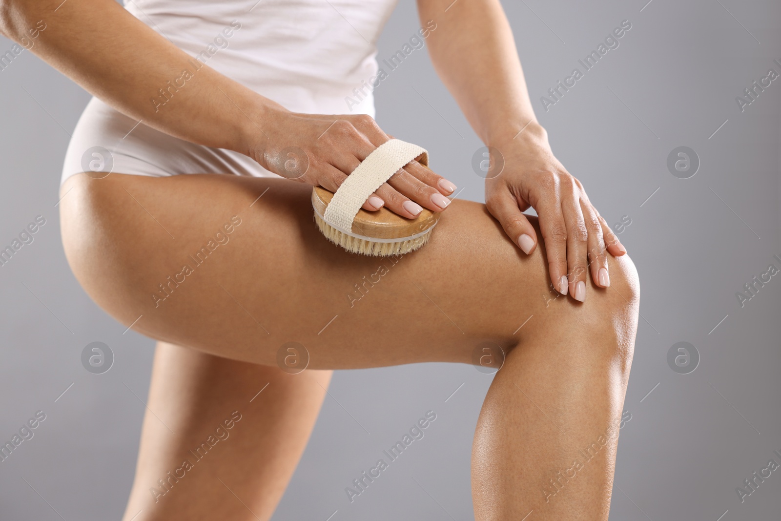 Photo of Woman doing anti cellulite massage with brush on grey background, closeup