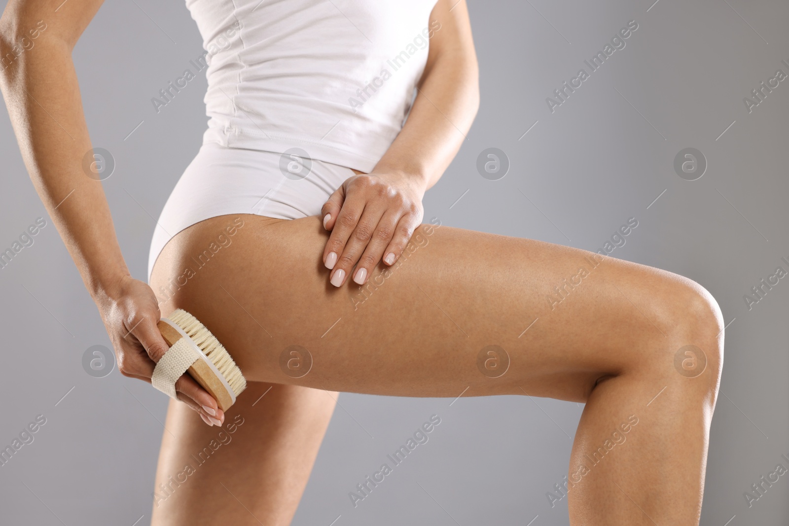 Photo of Woman doing anti cellulite massage with brush on grey background, closeup