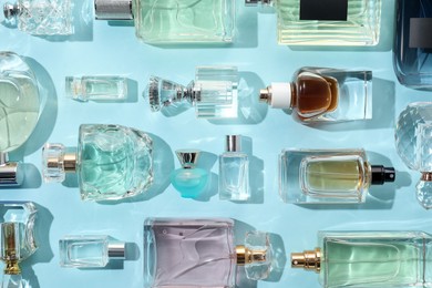 Photo of Bottles of various perfumes on light blue background, flat lay