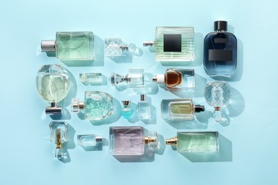 Photo of Bottles of various perfumes on light blue background, flat lay
