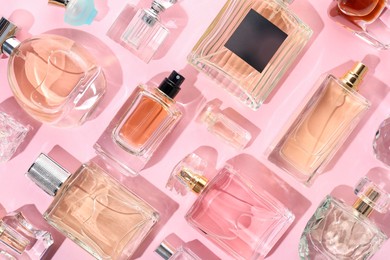 Photo of Bottles of various perfumes on pink background, flat lay