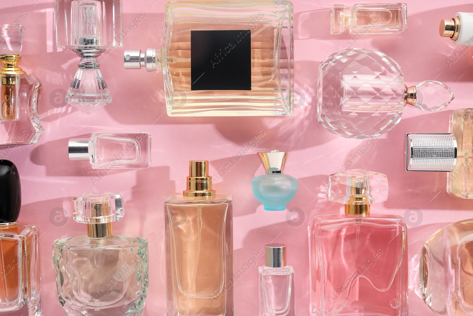 Bottles of various perfumes on pink background, flat lay Photo of Bottles of various perfumes on pink background, flat lay