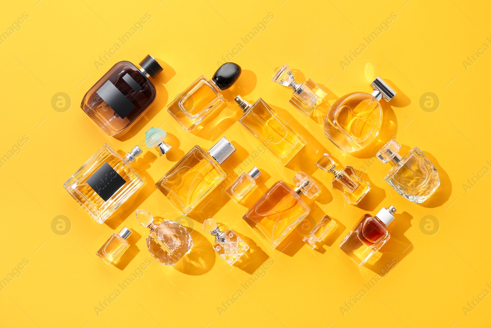 Bottles of various perfumes on yellow background, flat lay Photo of Bottles of various perfumes on yellow background, flat lay
