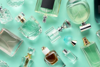 Photo of Bottles of various perfumes on turquoise background, flat lay