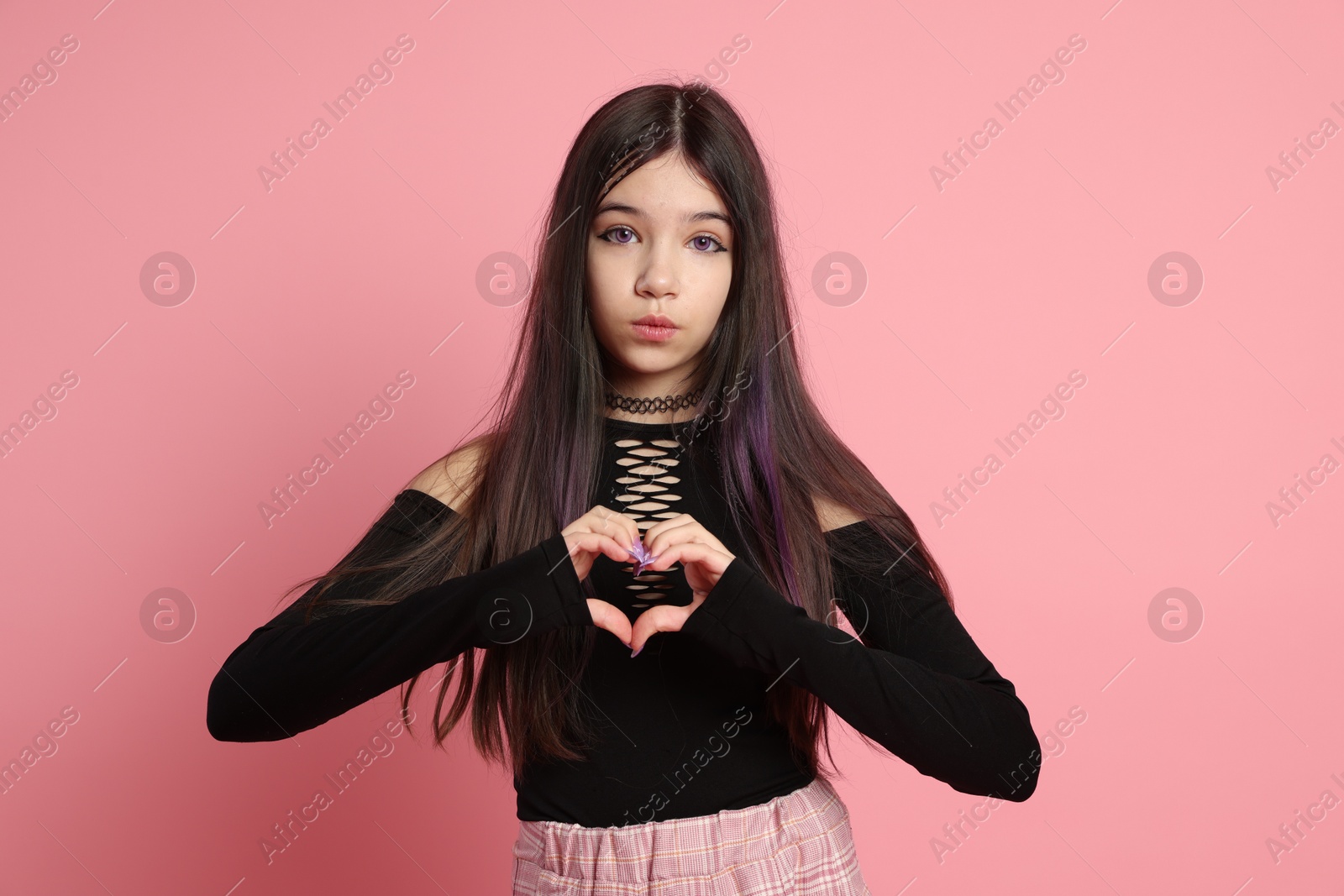 Photo of Teenage girl making heart gesture on pink background. Makeup and clothes in anime style