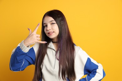 Teenage girl making rock gesture on orange background. Makeup in anime style