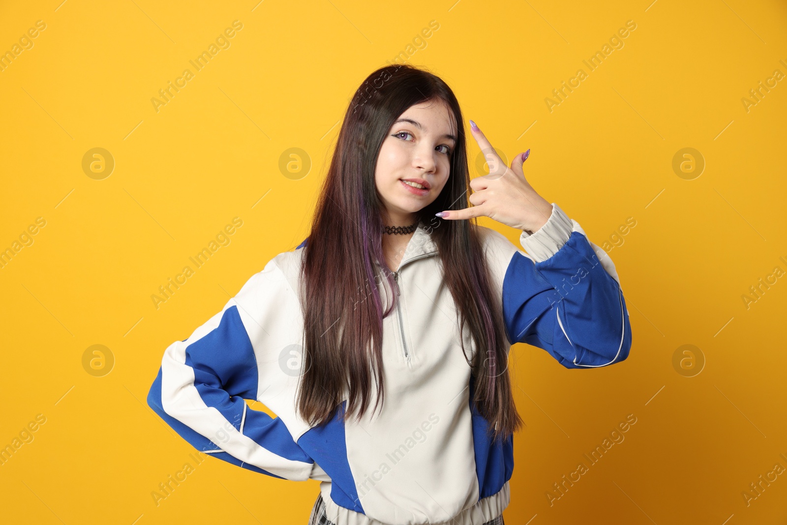 Photo of Teenage girl making rock gesture on orange background. Makeup in anime style