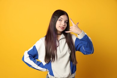 Photo of Teenage girl making rock gesture on orange background. Makeup in anime style