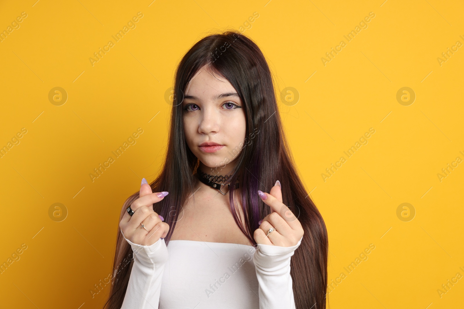 Photo of Teenage girl making finger heart gesture on orange background. Makeup in anime style