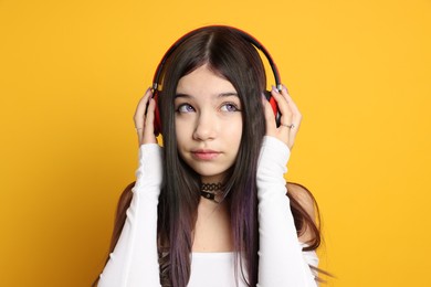 Photo of Teenage girl wearing stylish clothes and headphones on orange background. Makeup in anime style