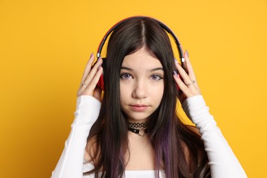 Photo of Teenage girl wearing stylish clothes and headphones on orange background. Makeup in anime style