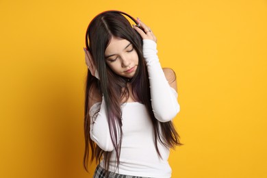 Teenage girl wearing stylish clothes and headphones on orange background. Makeup in anime style