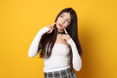 Photo of Teenage girl wearing stylish clothes and accessories on orange background. Makeup in anime style