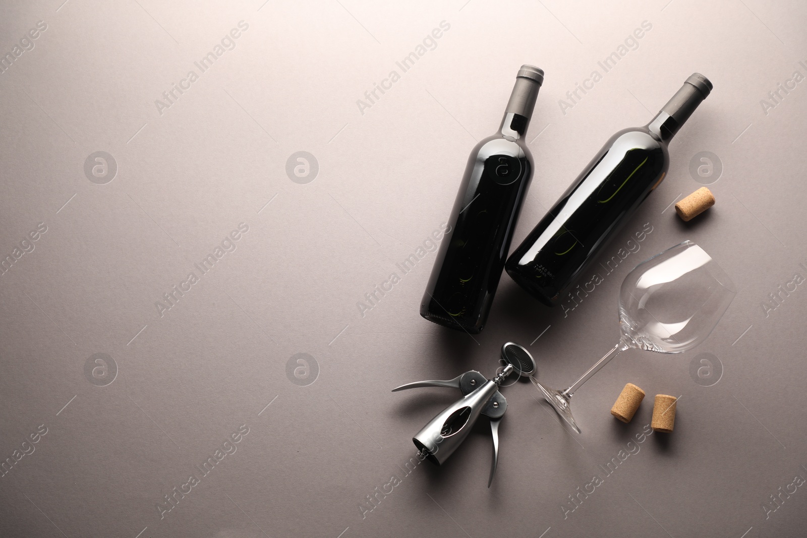Bottles of wine, glass, corks and wing corkscrew on light grey background, flat lay. Space for text Photo of Bottles of wine, glass, corks and wing corkscrew on light grey background, flat lay. Space for text