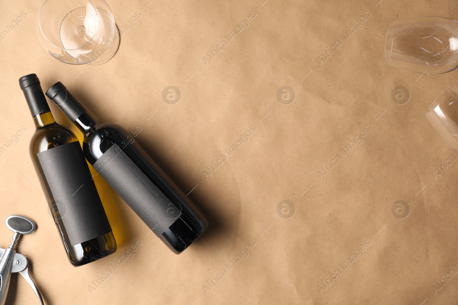 Bottles of wine, glasses and wing corkscrew on parchment paper, flat lay. Space for text Photo of Bottles of wine, glasses and wing corkscrew on parchment paper, flat lay. Space for text
