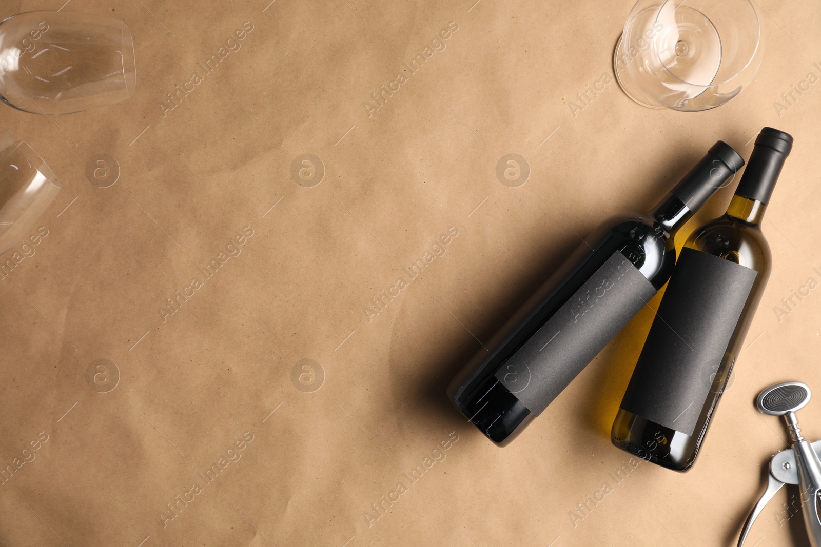 Bottles of wine, glasses and wing corkscrew on parchment paper, flat lay. Space for text Photo of Bottles of wine, glasses and wing corkscrew on parchment paper, flat lay. Space for text
