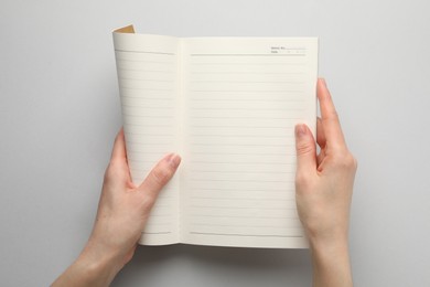 Photo of Woman with open copybook on light grey background, top view