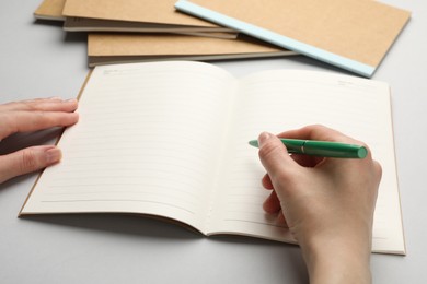 Photo of Woman writing in copybook on light grey background, closeup