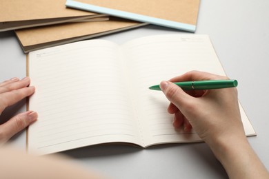 Photo of Woman writing in copybook on light grey background, closeup