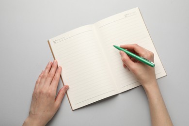 Photo of Woman writing in copybook on light grey background, top view