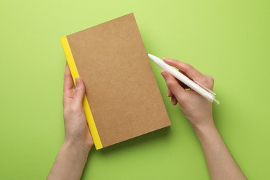 Photo of Woman with copybook and pen on green background, top view