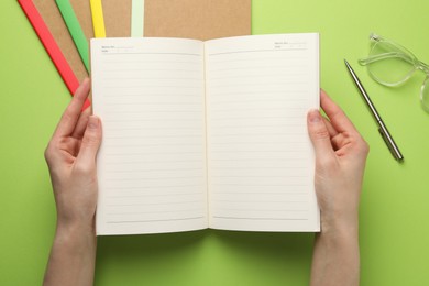 Photo of Woman with open copybook and other stationery on green background, top view