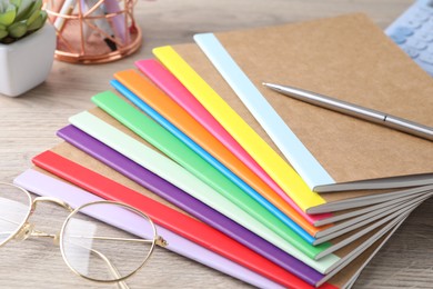 Photo of Different copybooks, pen and glasses on wooden table, closeup