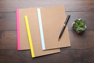 Photo of Different copybooks, pen and floral decor on wooden table, flat lay