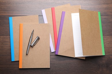 Photo of Different copybooks and fountain pen on wooden table, flat lay