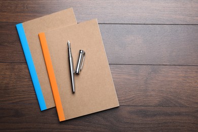 Photo of Copybooks and fountain pen on wooden table, top view. Space for text