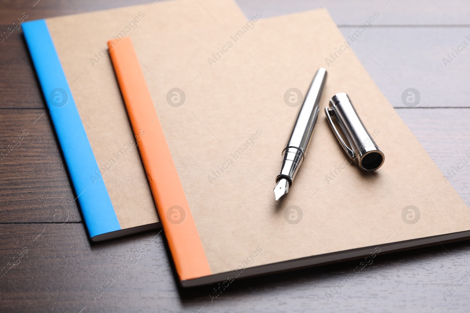 Photo of Copybooks and fountain pen on wooden table, closeup