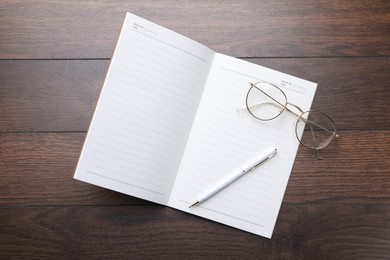 Photo of Open copybook, pen and glasses on wooden table, top view