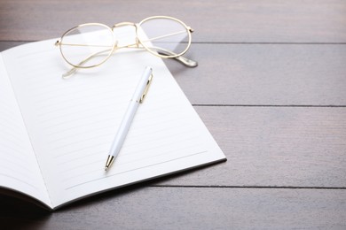 Photo of Open copybook, pen and glasses on wooden table, closeup. Space for text