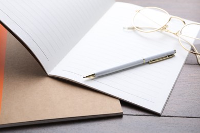 Photo of Copybooks, pen and glasses on wooden table, closeup