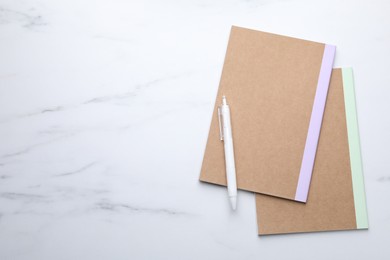 Photo of Copybooks and pen on white marble table, top view. Space for text