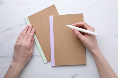 Photo of Woman with copybooks and pen at white marble table, top view