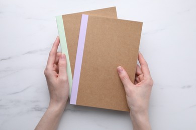 Photo of Woman with copybooks at white marble table, top view