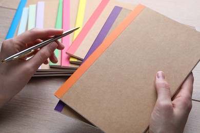 Photo of Woman with different copybooks and pen at wooden table, closeup