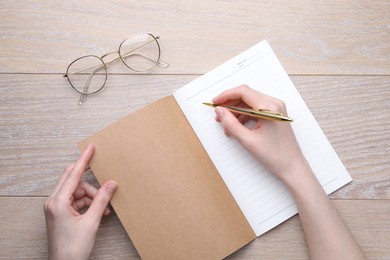 Photo of Woman writing in copybook at wooden table, top view