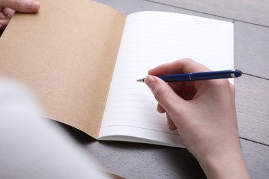 Photo of Woman writing in copybook at wooden table, closeup