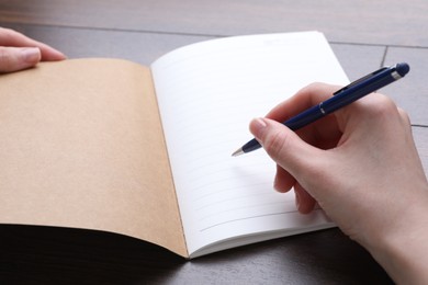 Photo of Woman writing in copybook at wooden table, closeup