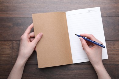 Photo of Woman writing in copybook at wooden table, top view