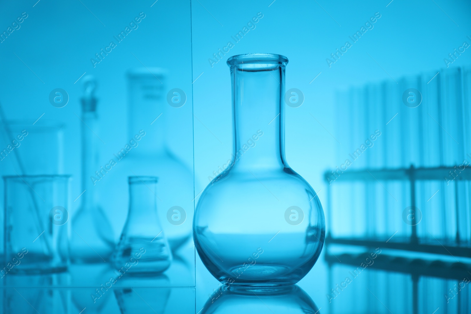 Photo of Laboratory glassware on mirror surface against light blue background