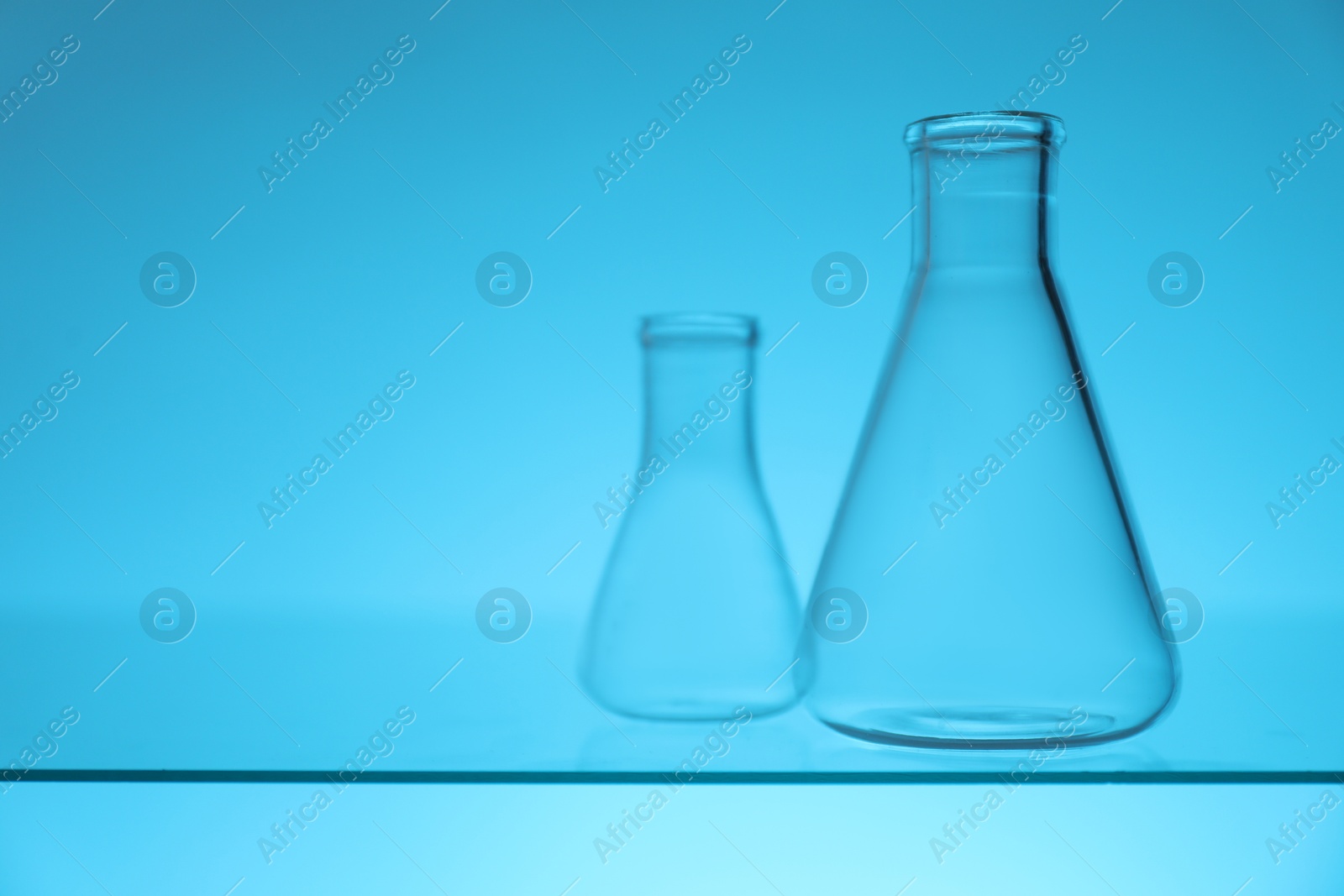 Photo of Empty flasks on glass surface against light blue background, space for text. Laboratory equipment