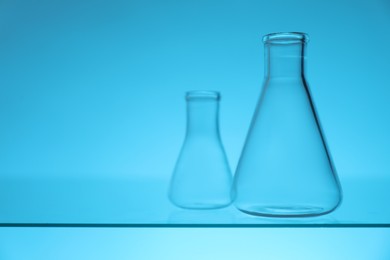 Photo of Empty flasks on glass surface against light blue background, space for text. Laboratory equipment